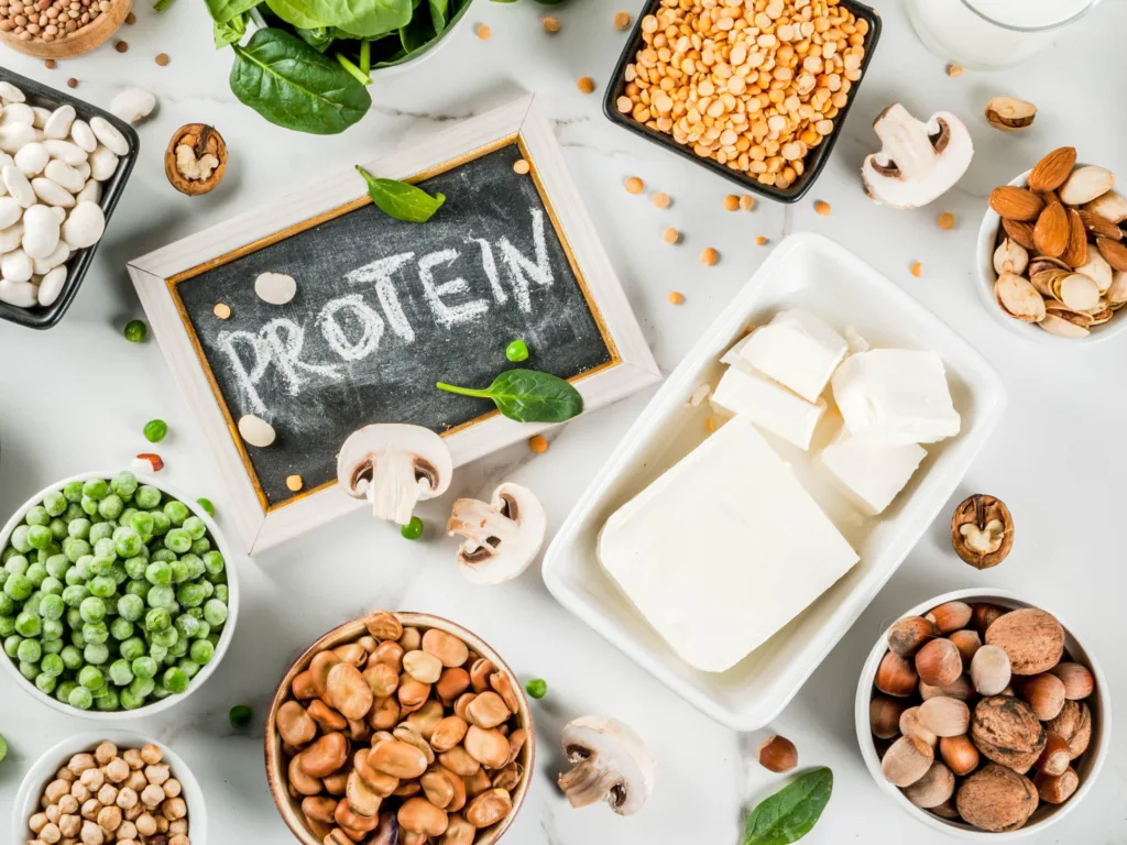 Protein written on a board with sources of plant-based proteins like pulses, tofu, peas, various nuts in bowls around it