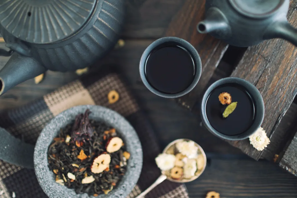 Tea blend in a mortar and pestle with pots and cups of black tea